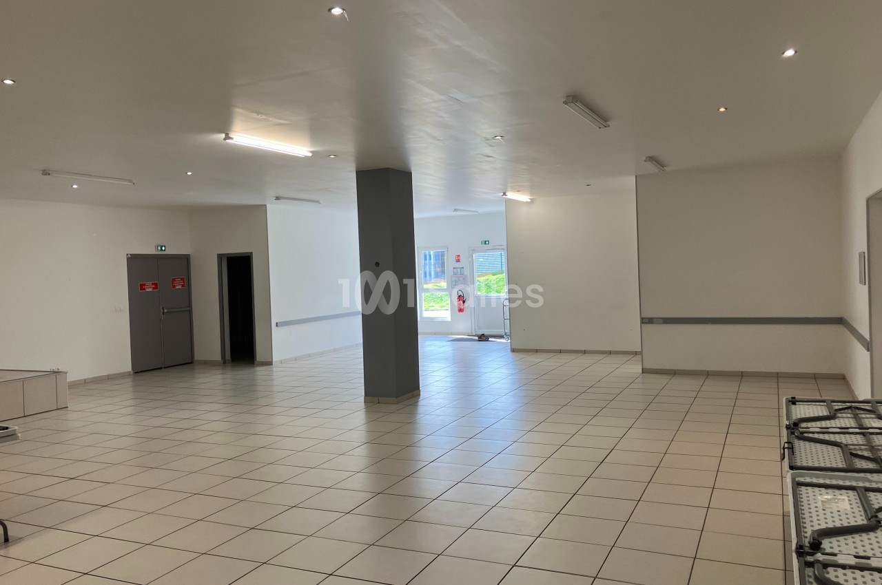 Salle vide avec carrelage clair, murs blancs, éclairage au plafond et porte vitrée donnant sur l'extérieur.