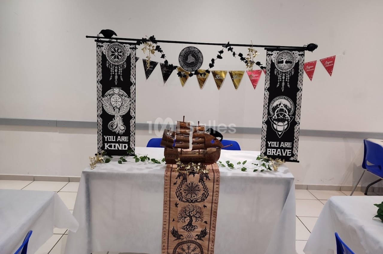 Décoration de table sur le thème marin avec un bateau en bois, bannières et guirlandes dans une salle lumineuse.