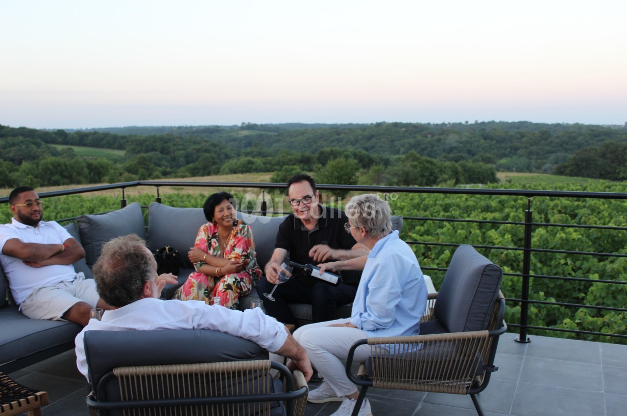 Un groupe de personnes discute et partage un moment convivial sur une terrasse surplombant un paysage verdoyant.