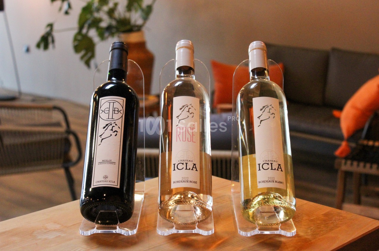 Trois bouteilles de vin Château Icla (rouge, rosé et blanc) posées sur une table en bois dans un intérieur chaleureux.