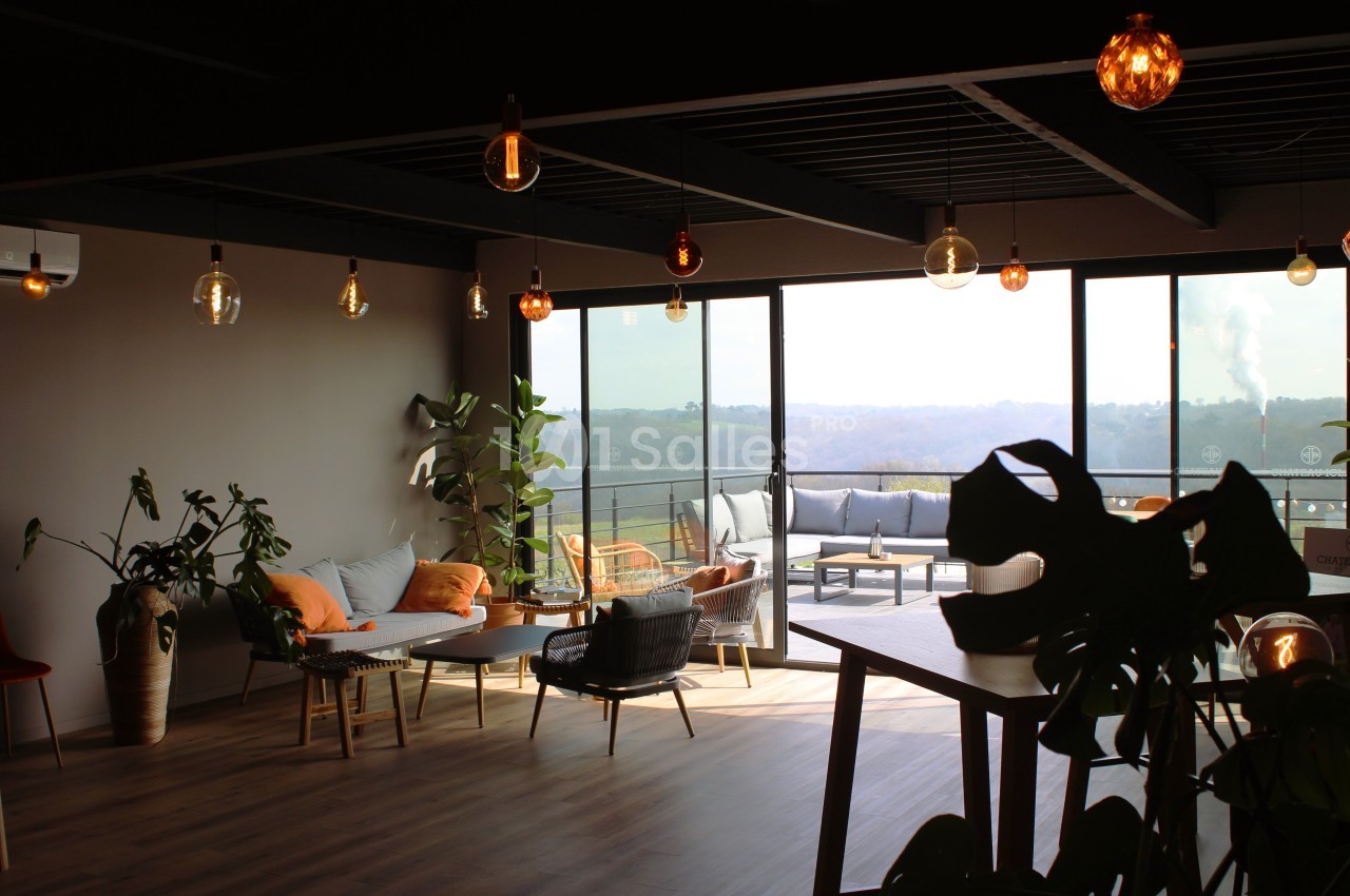Espace lumineux avec mobilier moderne, plantes d'intérieur et grandes baies vitrées donnant sur une terrasse et un paysage.