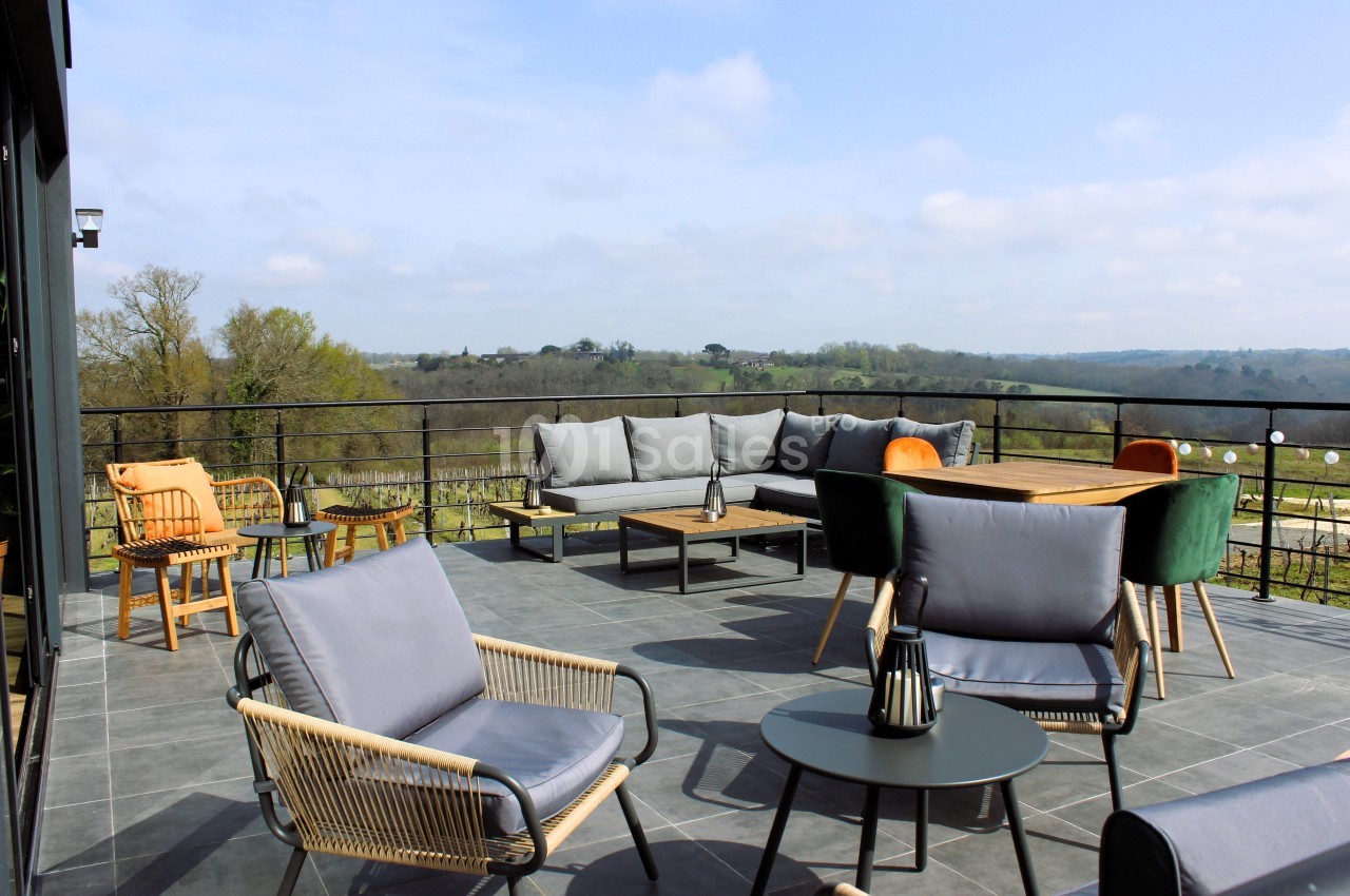 Terrasse spacieuse avec mobilier de jardin moderne, vue dégagée sur une campagne verdoyante sous un ciel partiellement…