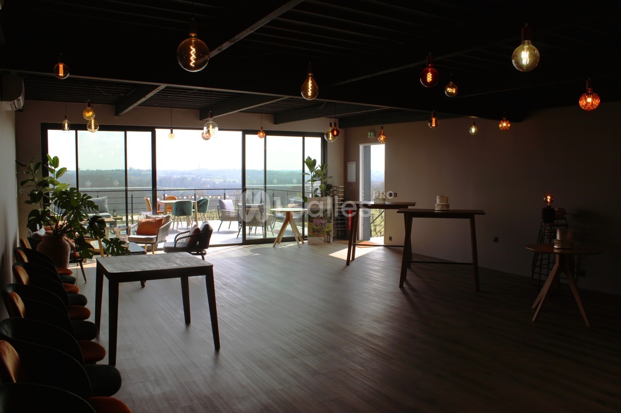 Salle lumineuse avec grandes baies vitrées, mobilier minimaliste et suspensions décoratives au plafond.