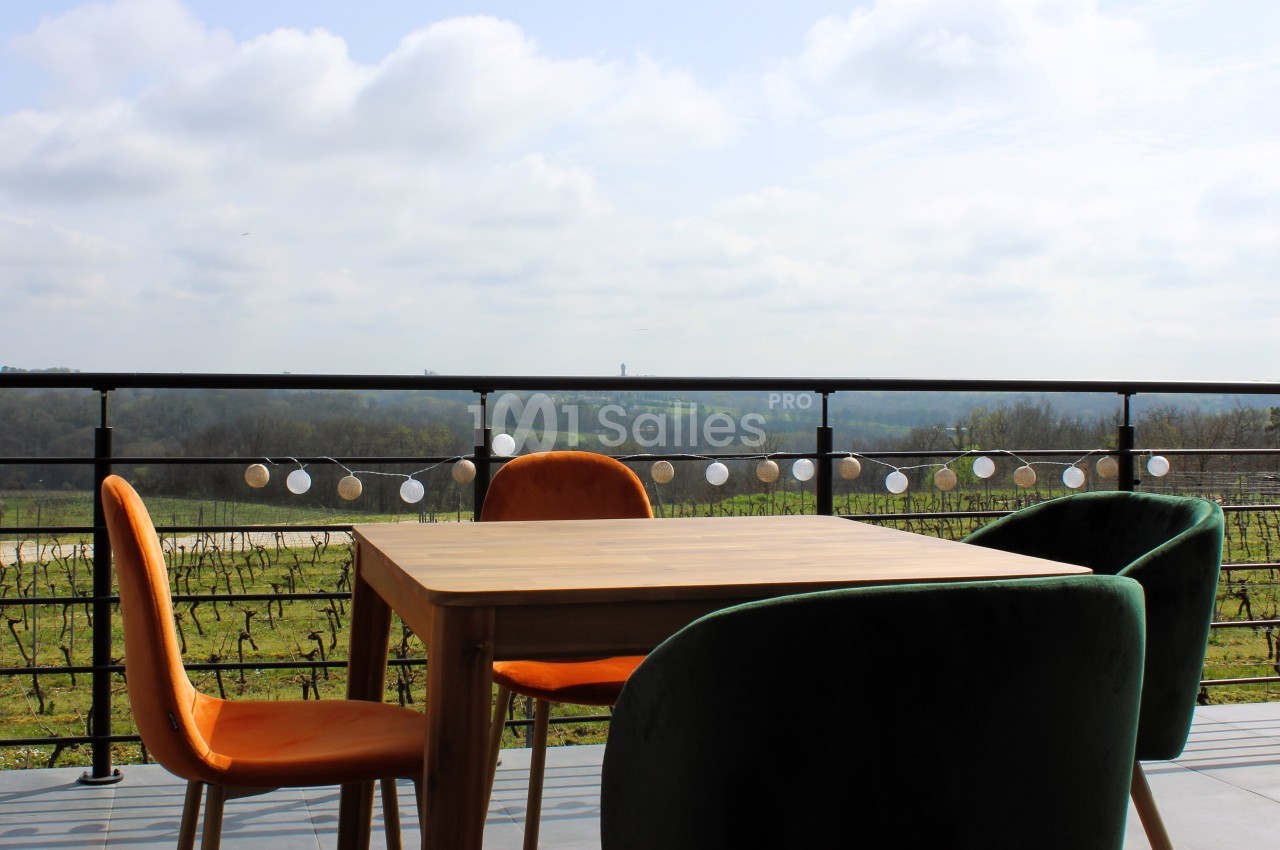 Table et chaises colorées sur une terrasse avec vue dégagée sur la campagne et une guirlande lumineuse accrochée.