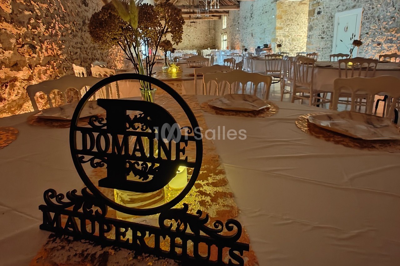 Salle de réception décorée avec des tables dressées et un panneau indiquant ’Domaine Mauperthuis’ au premier plan.