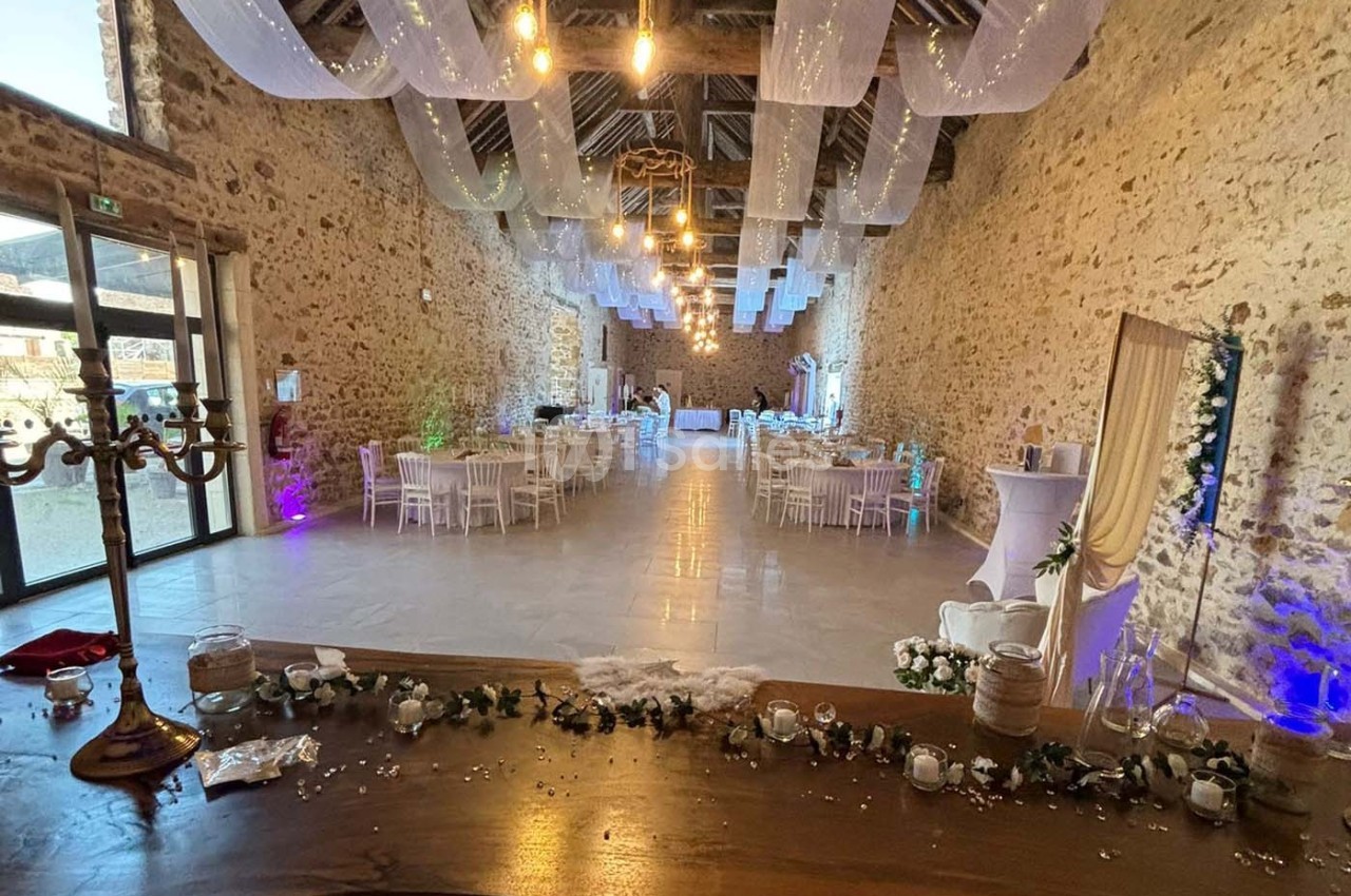Salle de réception en pierre avec tables rondes dressées, décorations lumineuses et voilages suspendus au plafond.