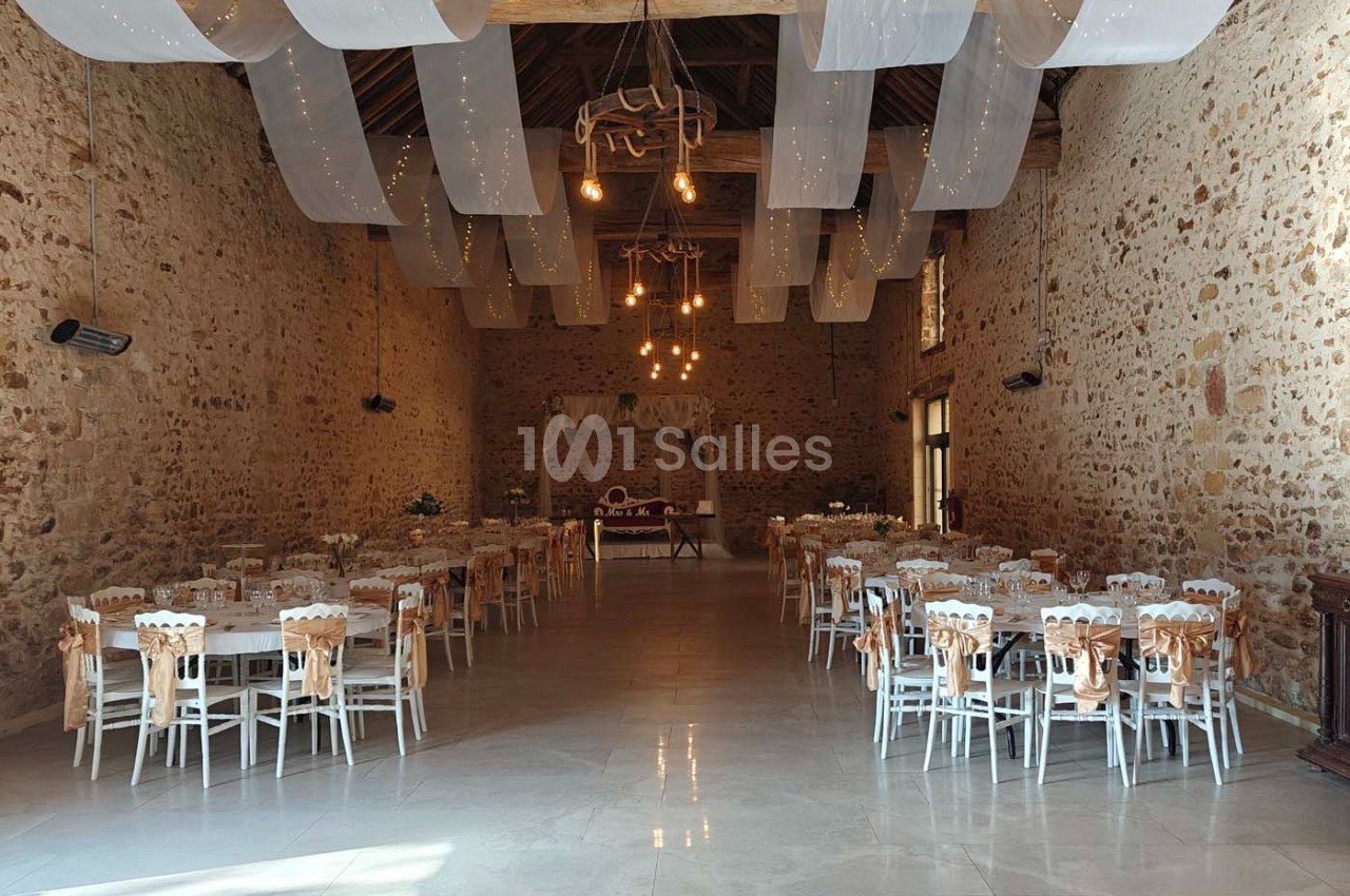Salle de réception en pierre avec tables et chaises décorées, éclairée par des guirlandes lumineuses suspendues.