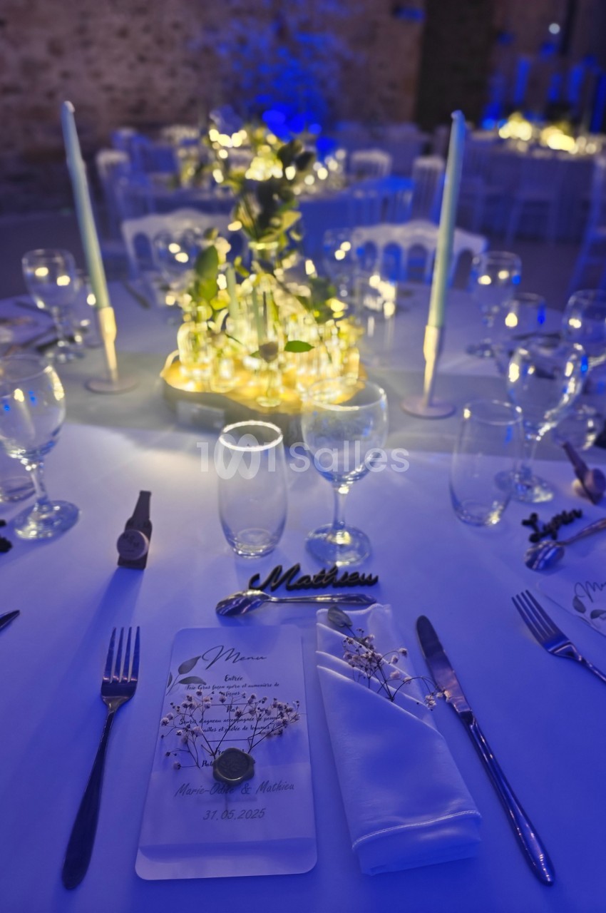 Table de réception élégamment dressée avec des bougies, des verres, un menu et une décoration florale lumineuse.