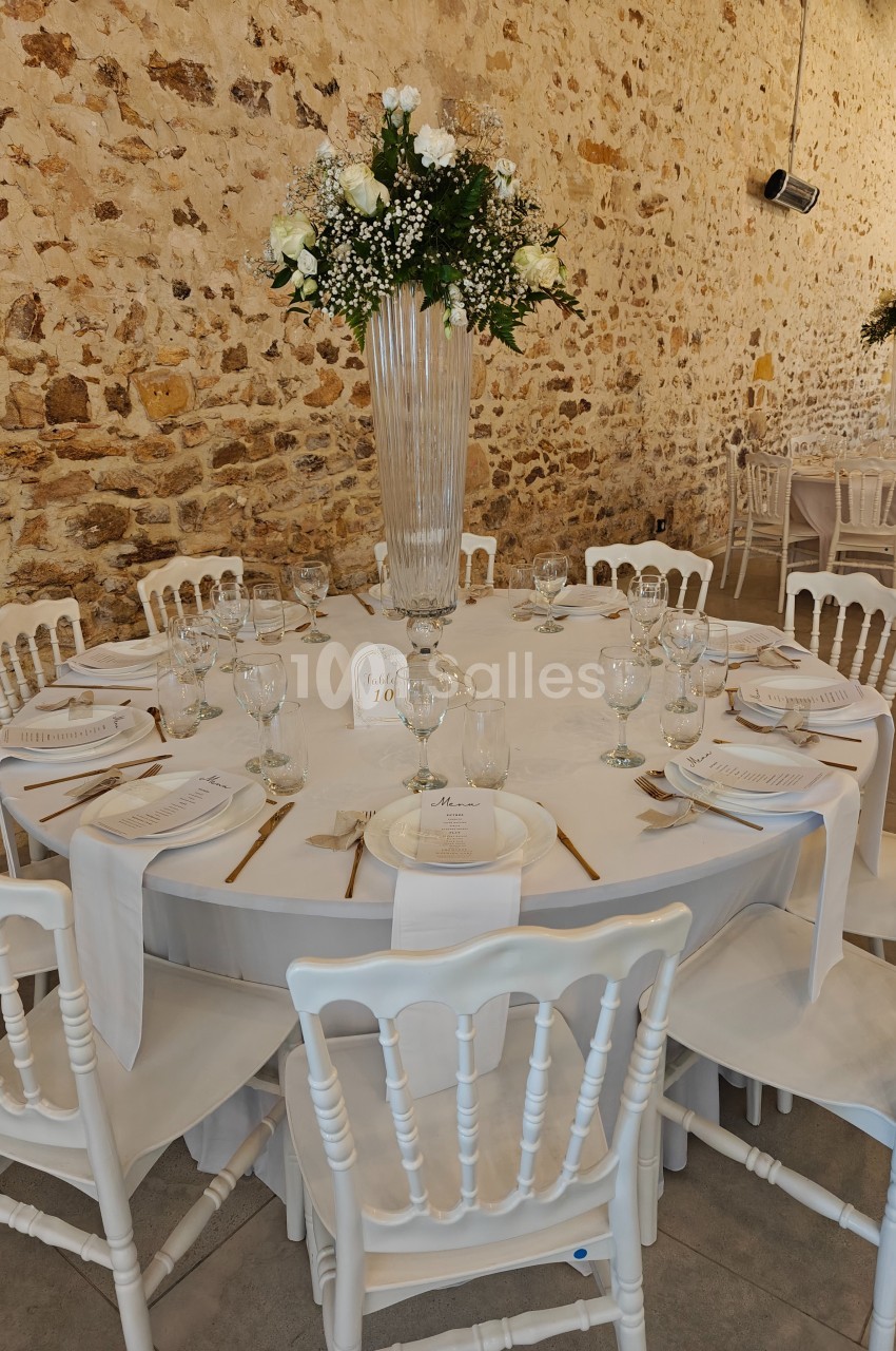 Table ronde décorée pour un événement, avec nappes blanches, vaisselle élégante et centre de table floral dans une salle en…