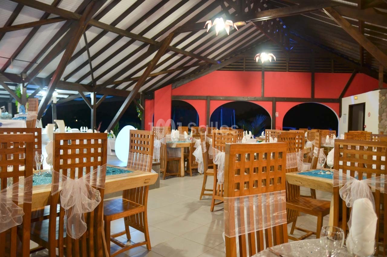 Salle de restaurant avec des tables dressées, des chaises en bois et une décoration lumineuse sous un toit en charpente.
