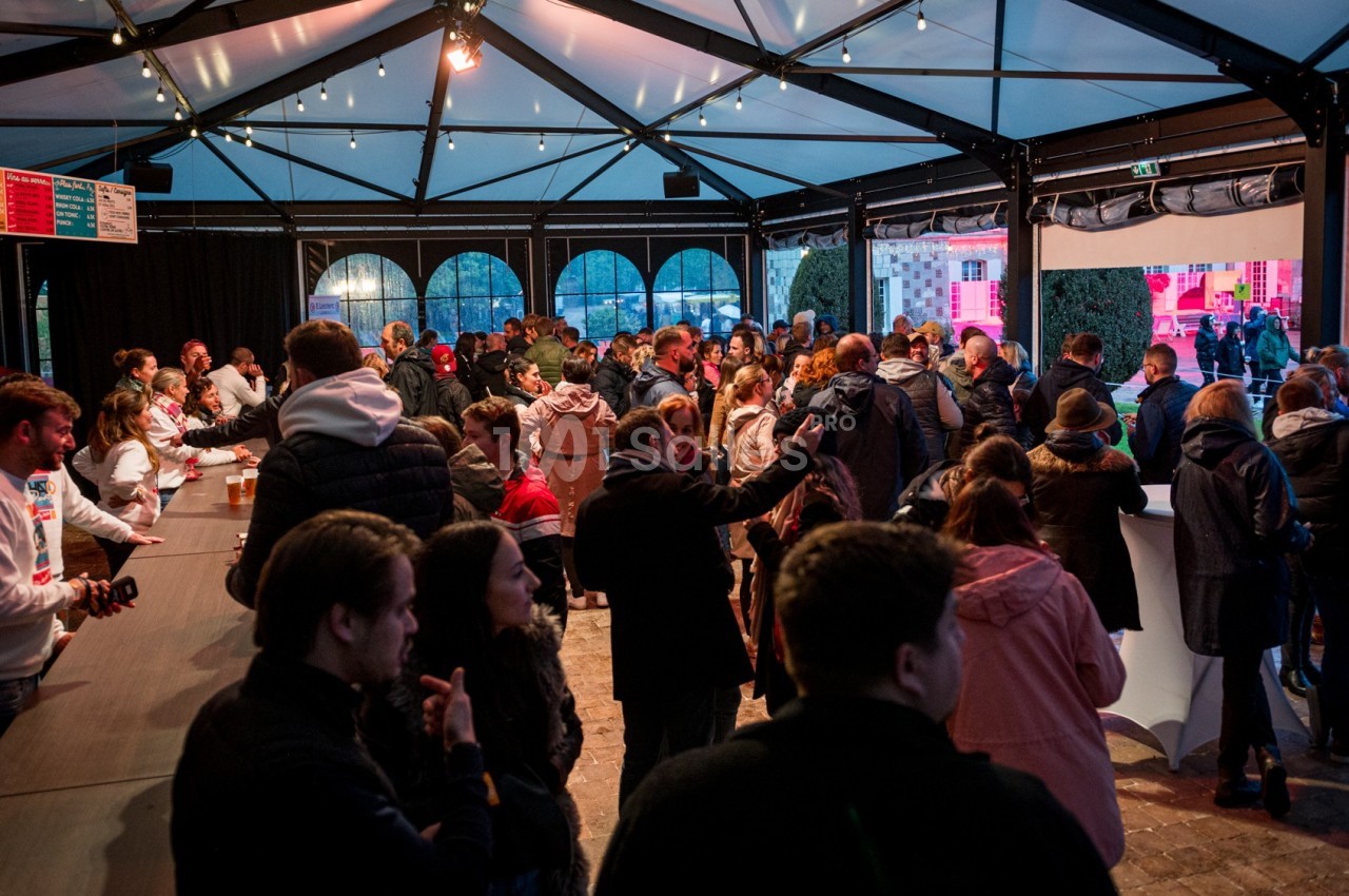 Groupe de personnes rassemblées sous une structure couverte, près d'un comptoir, dans une ambiance conviviale.