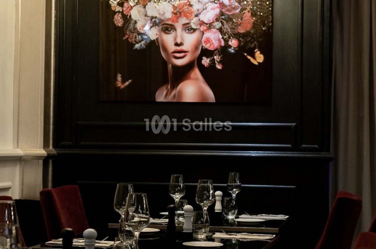 Table dressée dans un restaurant élégant, avec un tableau représentant une femme ornée de fleurs en arrière-plan.