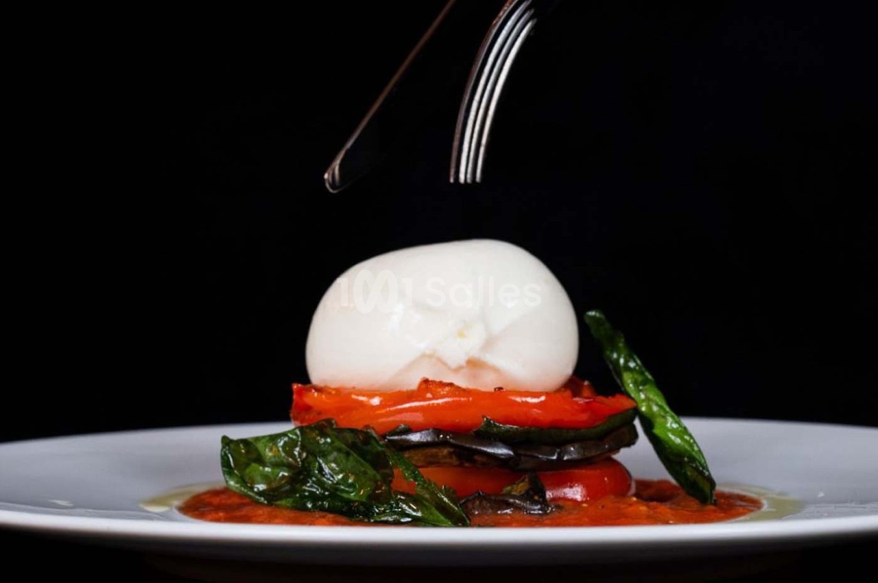 Assiette de légumes grillés superposés avec une boule de mozzarella, garnie de feuilles de basilic et sauce tomate.