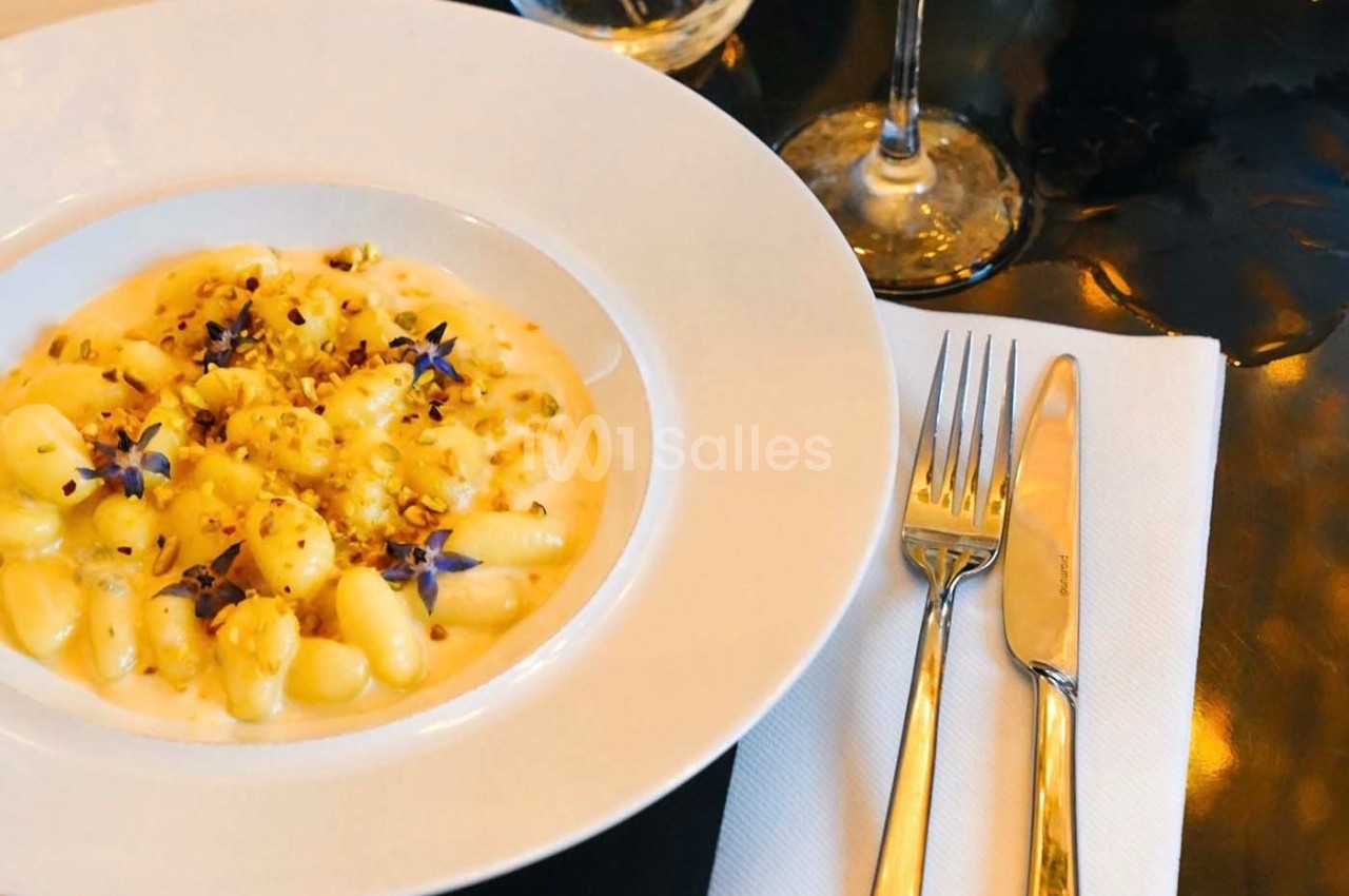 Assiette de gnocchis crémeux garnis de fleurs comestibles et éclats de noix, servie sur une table élégante.