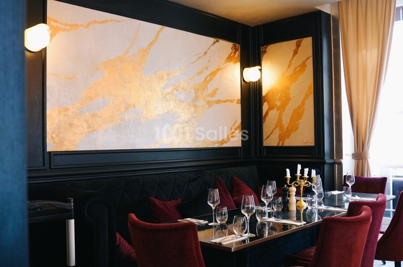 Salle de restaurant élégante avec banquettes noires, chaises rouges, table dressée et murs décorés de motifs dorés.