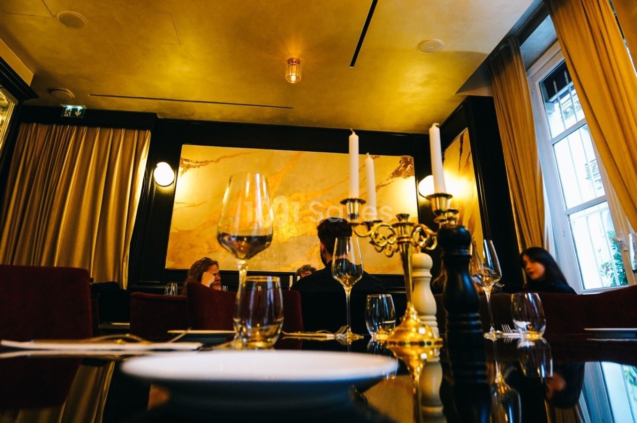 Salle de restaurant élégante avec des murs dorés, des chandeliers et des tables dressées avec des verres et assiettes.