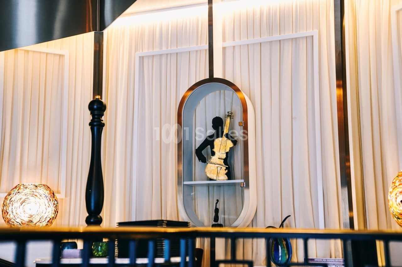 Statue noire d'un musicien jouant du violon, exposée dans une niche éclairée devant un rideau beige.