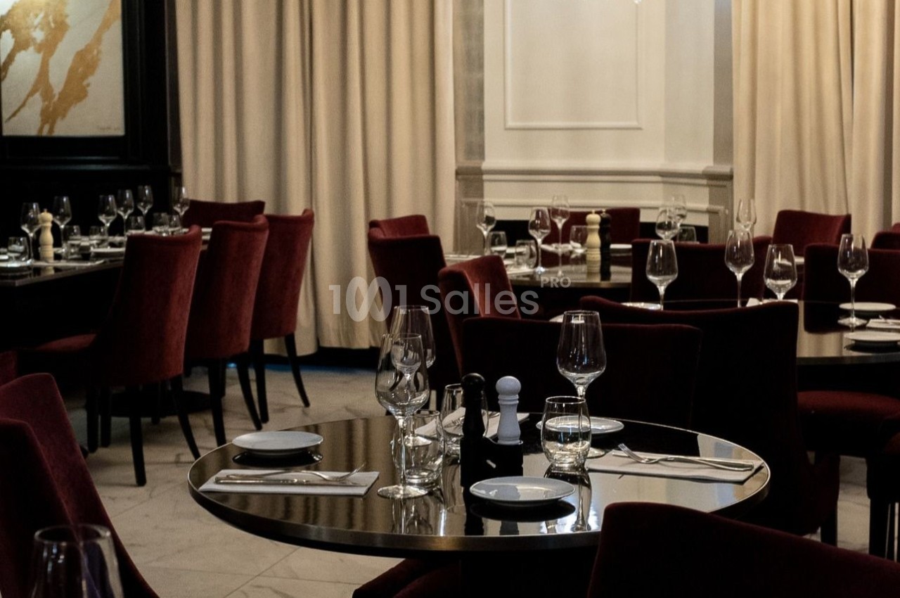 Salle de restaurant élégante avec tables dressées, nappes blanches, verres et chaises en velours rouge.