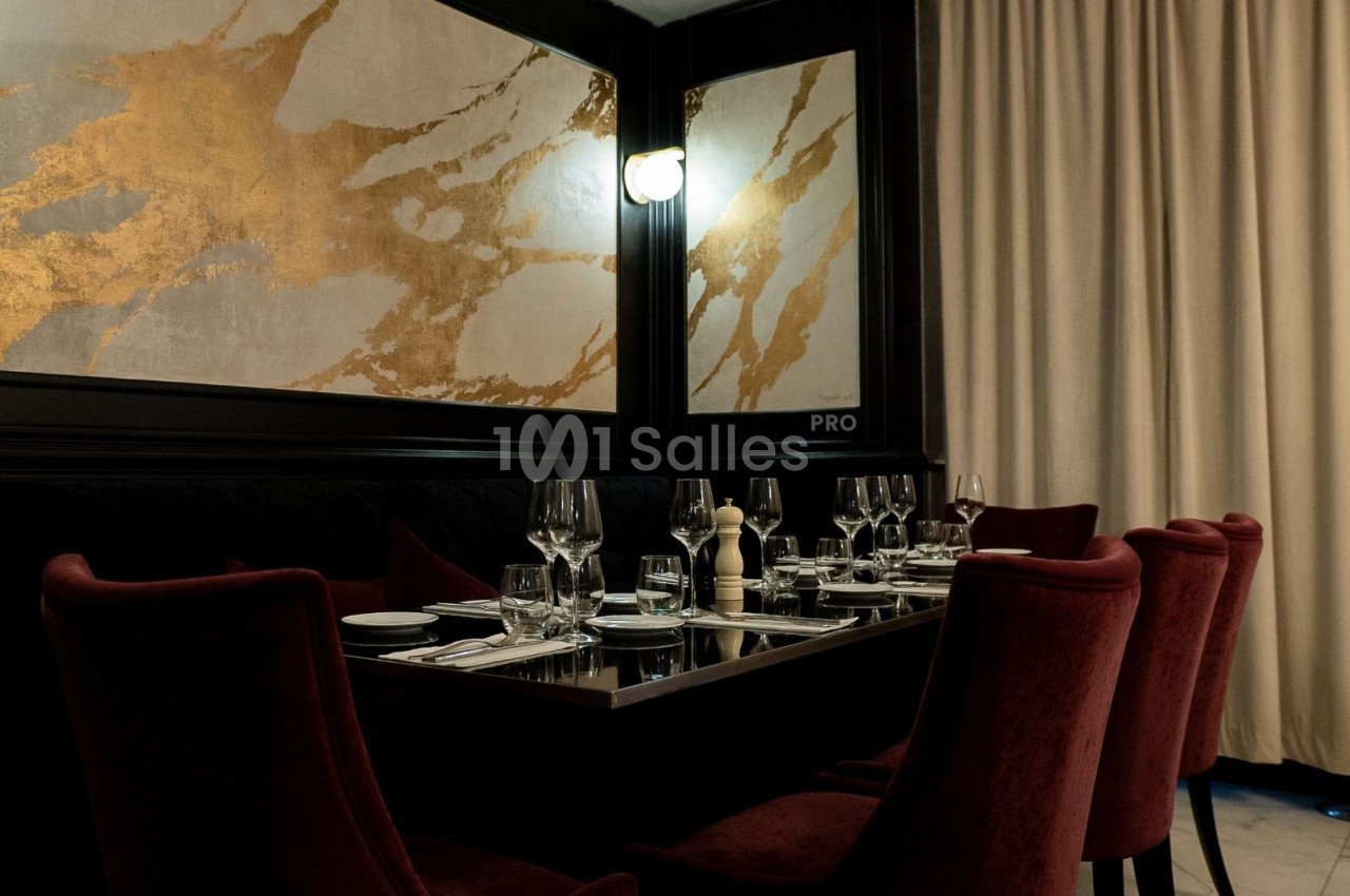 Salle de restaurant élégante avec table dressée, chaises en velours rouge et décor mural doré.