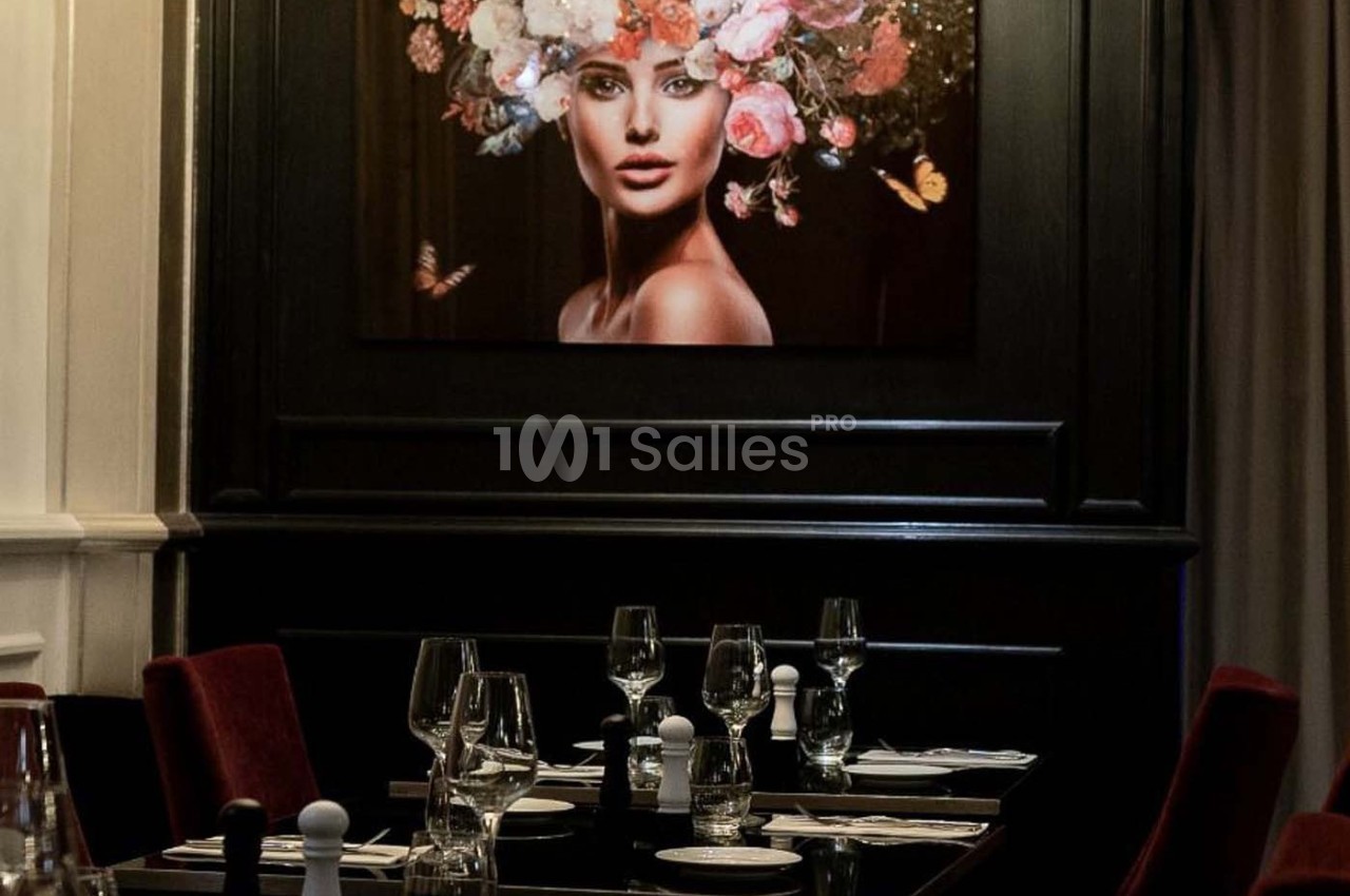 Table dressée dans un restaurant élégant avec un tableau représentant une femme ornée de fleurs en arrière-plan.
