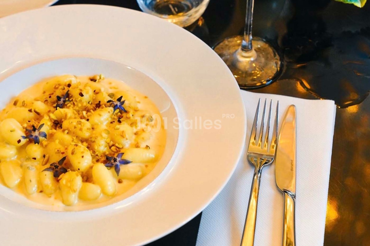 Assiette de gnocchis crémeux garnis de fleurs comestibles et éclats de noix, servie sur une table élégante.