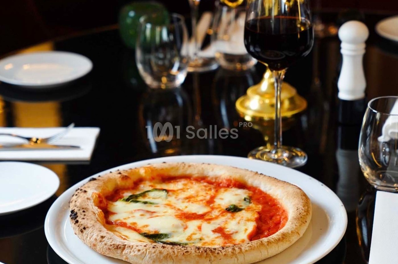 Pizza margherita servie sur une table élégante avec un verre de vin rouge et des couverts.
