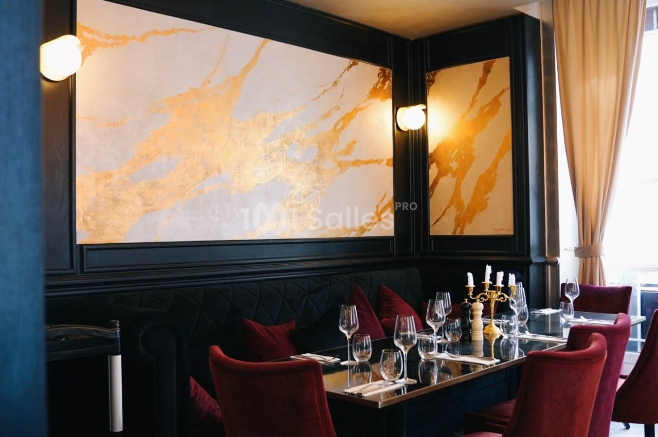 Salle de restaurant élégante avec banquettes noires, chaises rouges, table dressée et mur décoré de motifs dorés.