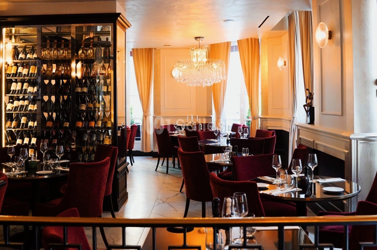 Salle de restaurant élégante avec chaises rouges, tables dressées et éclairage chaleureux sous un lustre.