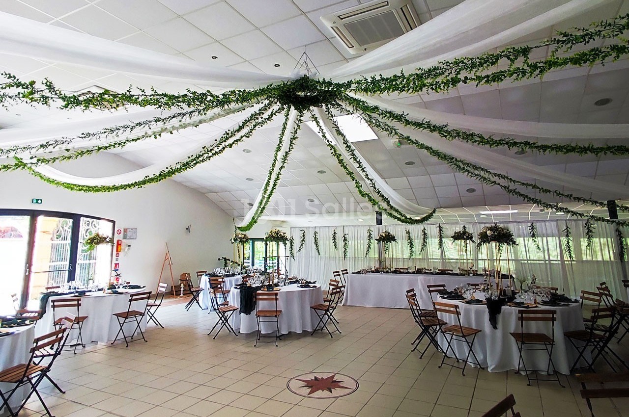 Salle de réception décorée avec des guirlandes végétales suspendues et des tables dressées pour un événement.