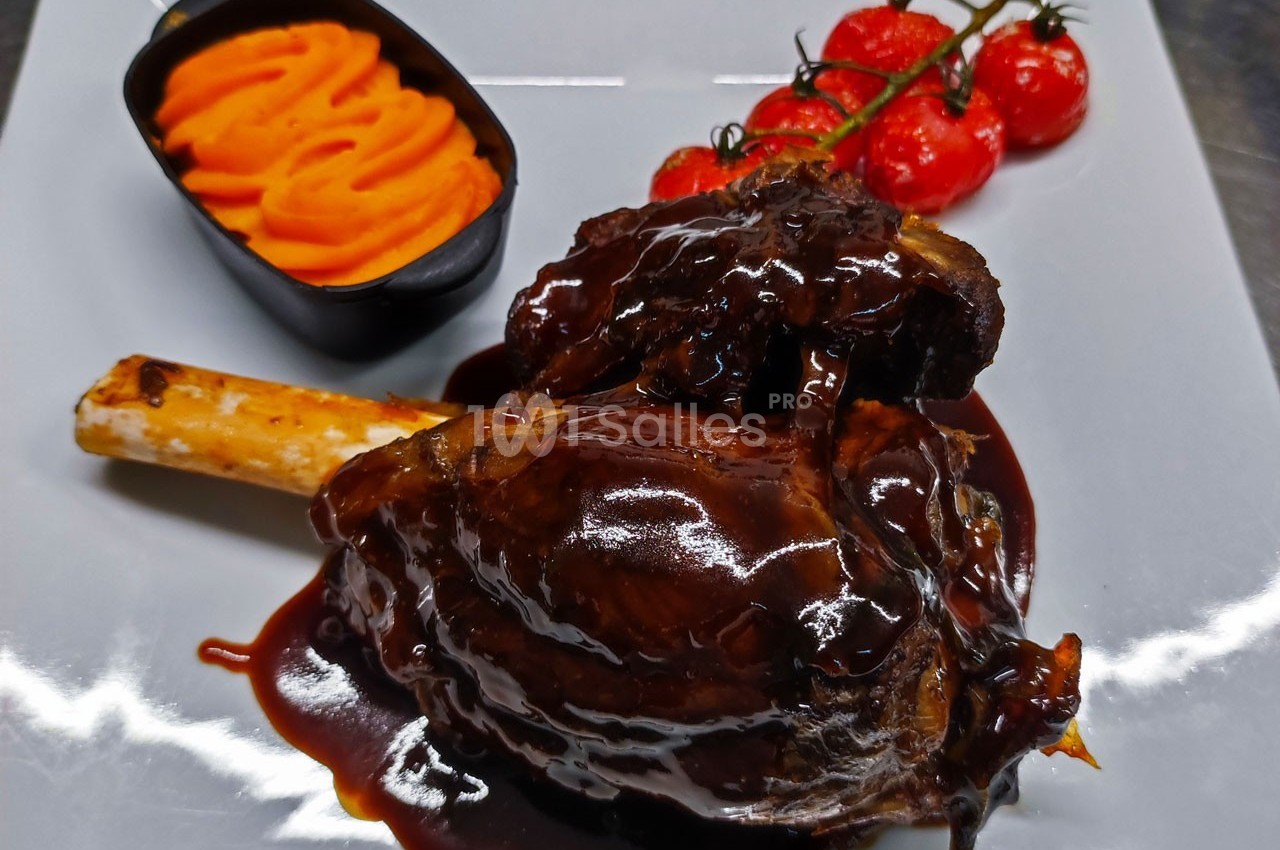 Jarret d'agneau nappé de sauce brune, accompagné de purée de patate douce et de tomates cerises rôties.