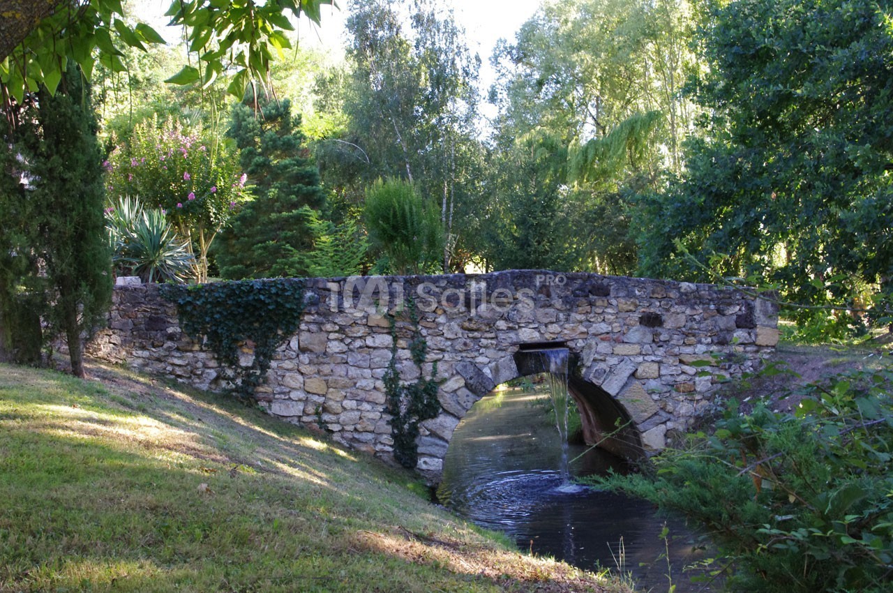 Pont en pierre ancienne enjambant un petit cours d'eau entouré de végétation verdoyante.