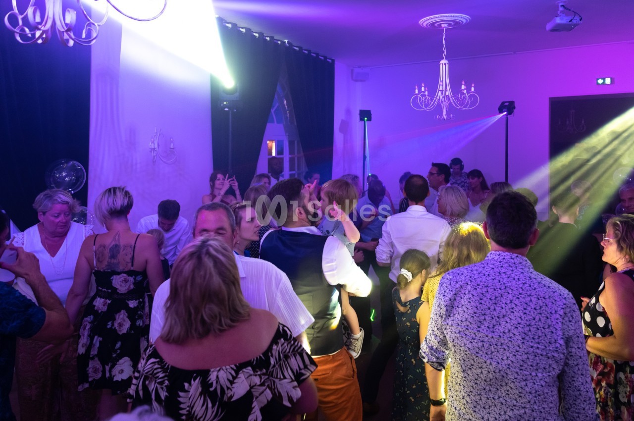 Groupe de personnes dansant et discutant dans une salle éclairée par des lumières colorées.