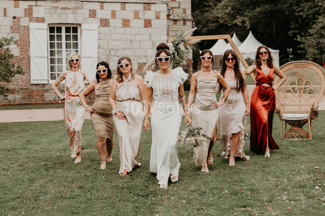 Un groupe de femmes en tenues élégantes et lunettes de soleil marche sur une pelouse devant un bâtiment en pierre.