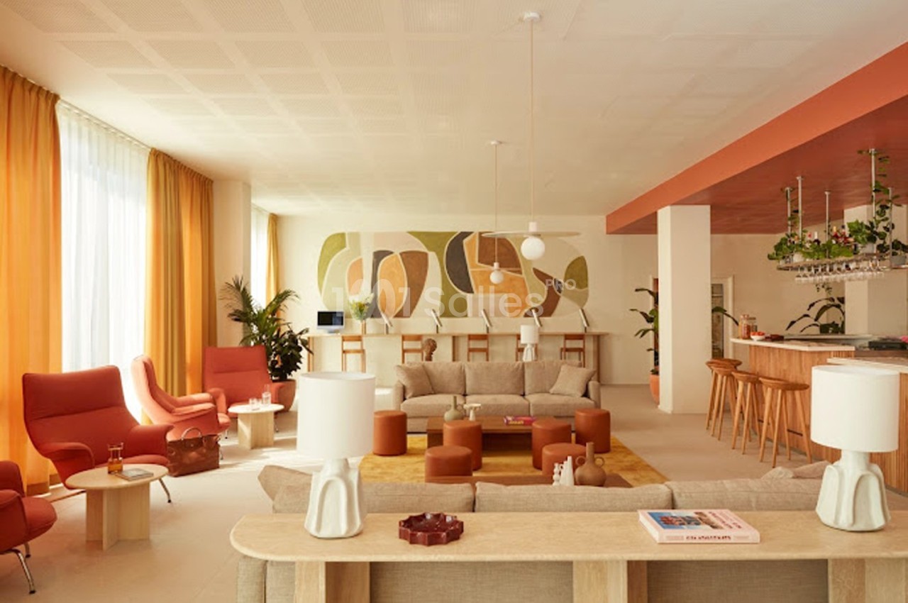 Salon lumineux avec mobilier moderne, canapés beiges, fauteuils orange, plantes et bar en bois dans un décor chaleureux.