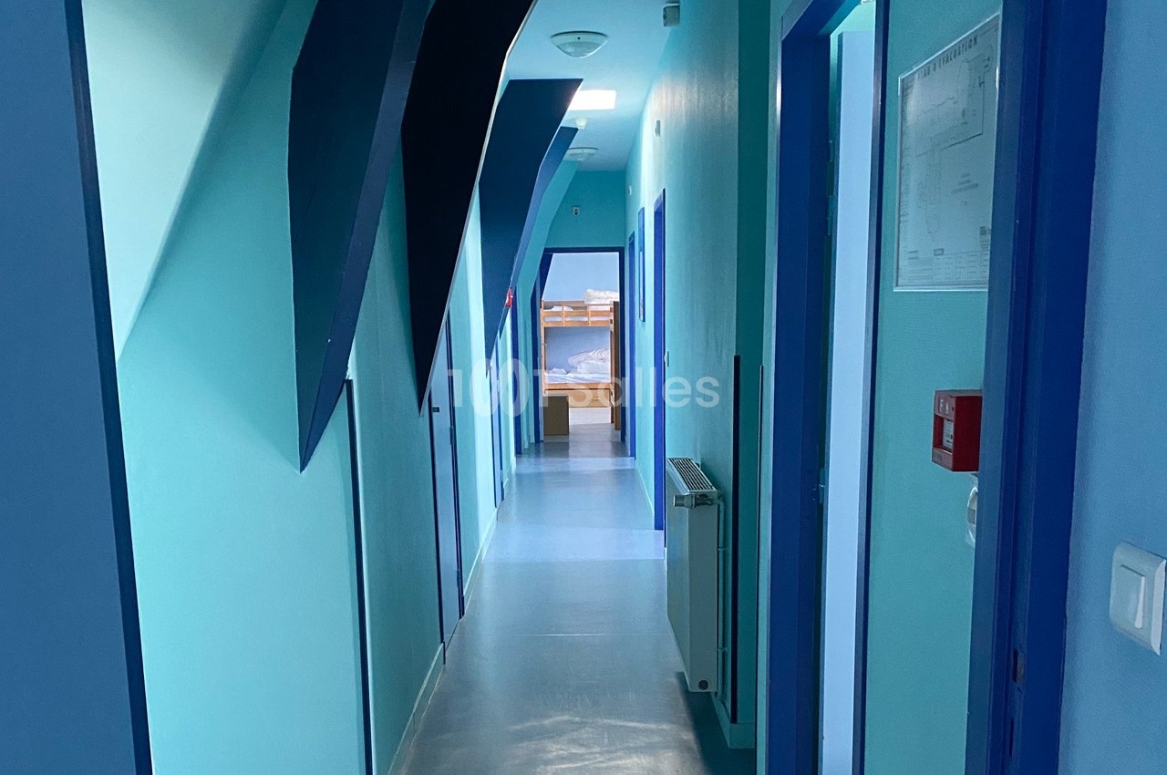 Couloir intérieur avec murs bleus, portes alignées des deux côtés et lumière naturelle au fond.