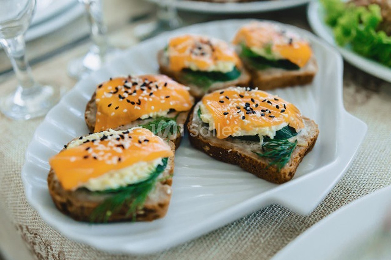 Tranches de pain garnies de fromage, saumon fumé, aneth et graines de sésame, servies sur une assiette blanche.