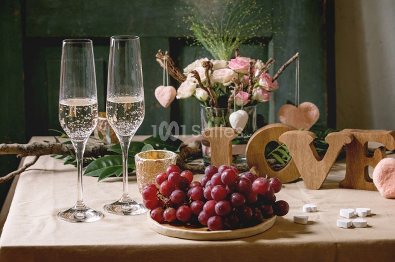Deux flûtes de champagne, une assiette de raisins et une décoration florale sur une table élégamment dressée.