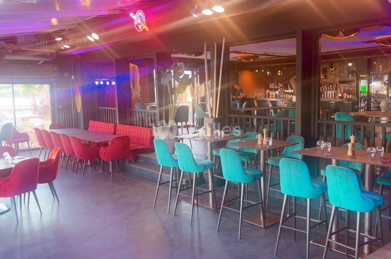 Salle de restaurant moderne avec tables en bois, chaises colorées et bar en arrière-plan.