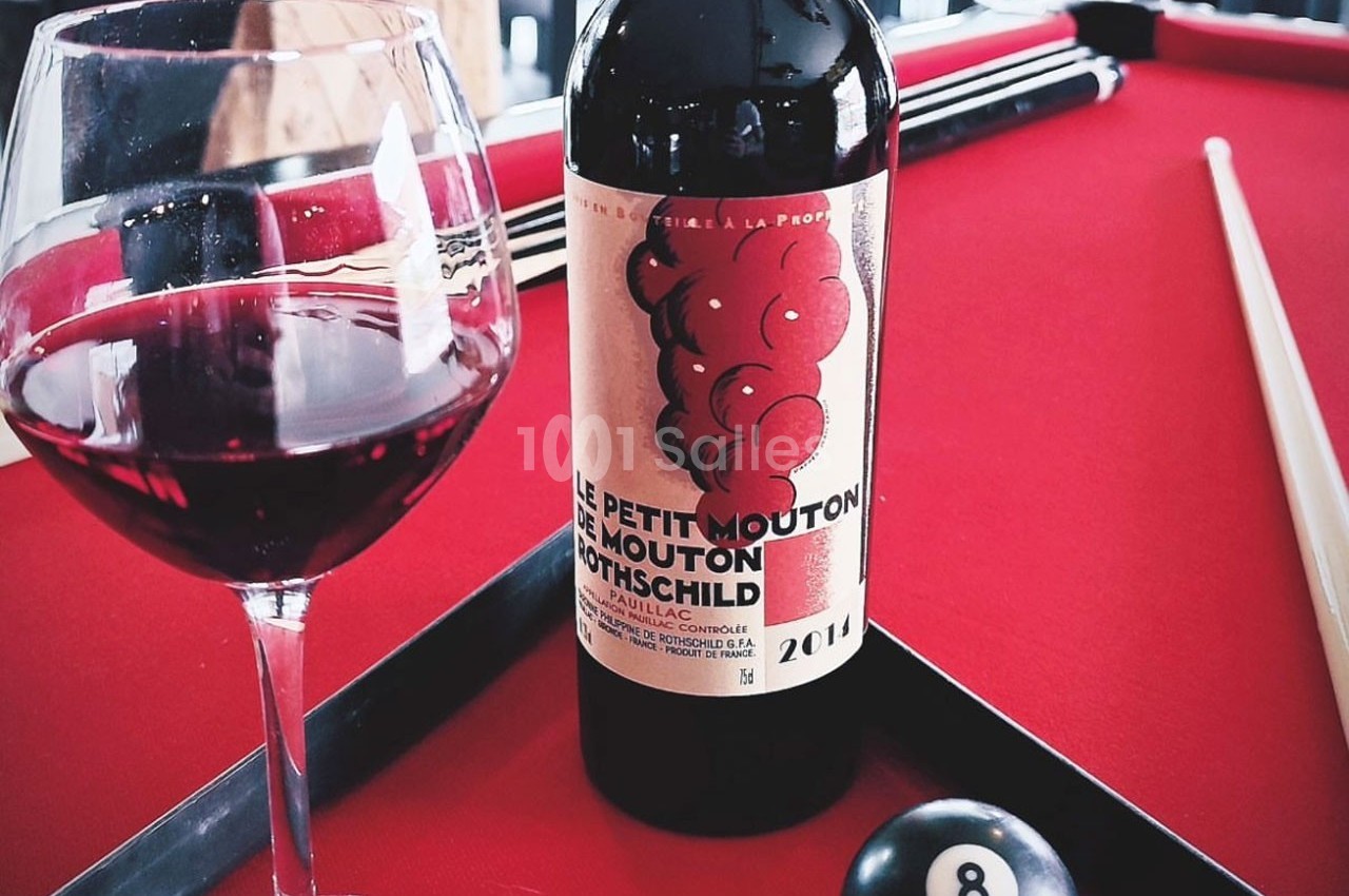 Bouteille de vin rouge et verre de vin posés sur une table de billard rouge avec une bille numéro 8.