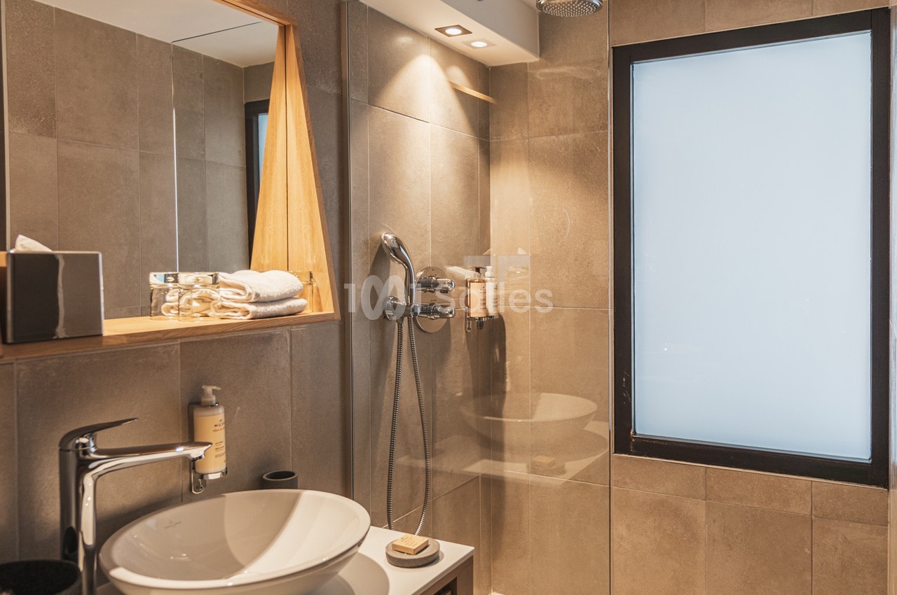 Salle de bain moderne avec douche à l'italienne, lavabo blanc, miroir encadré en bois et fenêtre opaque.