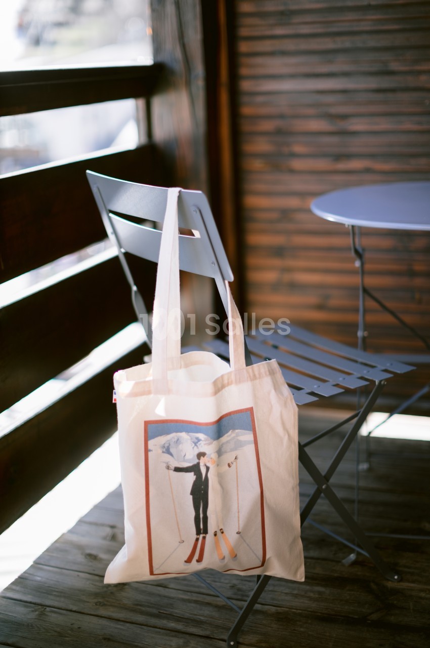 Sac en toile avec illustration de skieurs suspendu à une chaise en métal sur une terrasse en bois.