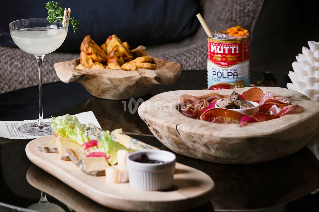 Assortiment de plats comprenant charcuterie, légumes, pain, pommes de terre et un cocktail sur une table en bois.
