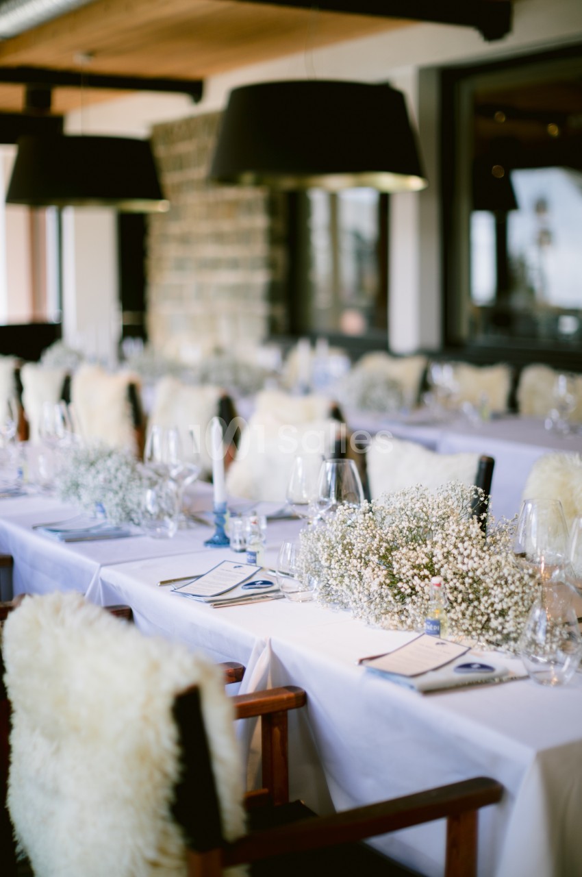 Table dressée avec nappes blanches, chaises couvertes de fourrure, décorations florales et bougies dans un intérieur élégant.