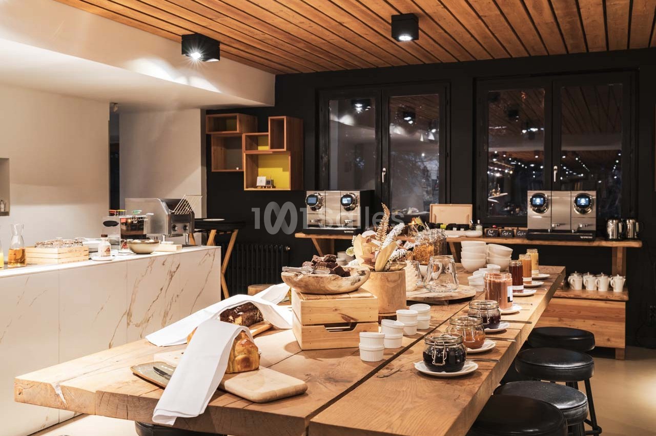 Buffet de petit-déjeuner avec pains, confitures, céréales et boissons, présenté sur une table en bois dans une salle…