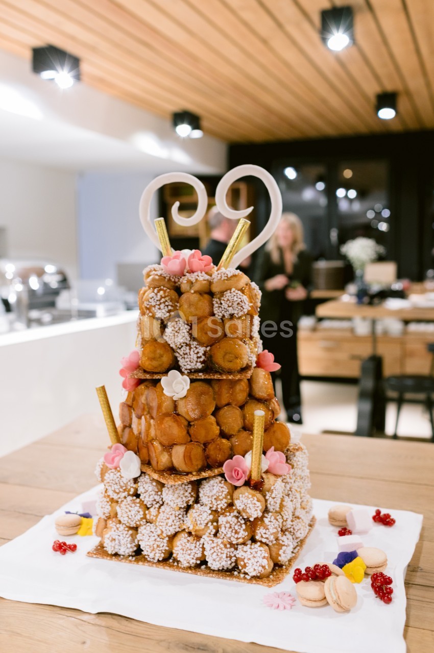 Pièce montée en choux décorée de fleurs en sucre, spirales en chocolat et macarons, posée sur une table en bois.