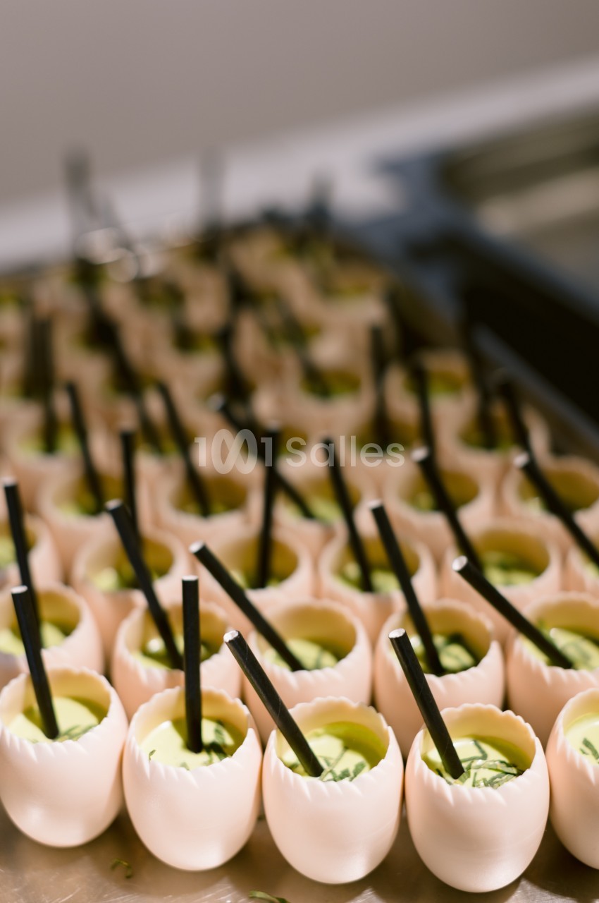 Des coquilles d'œufs remplies d'une mousse verte, chacune avec une paille noire, alignées sur un plateau.