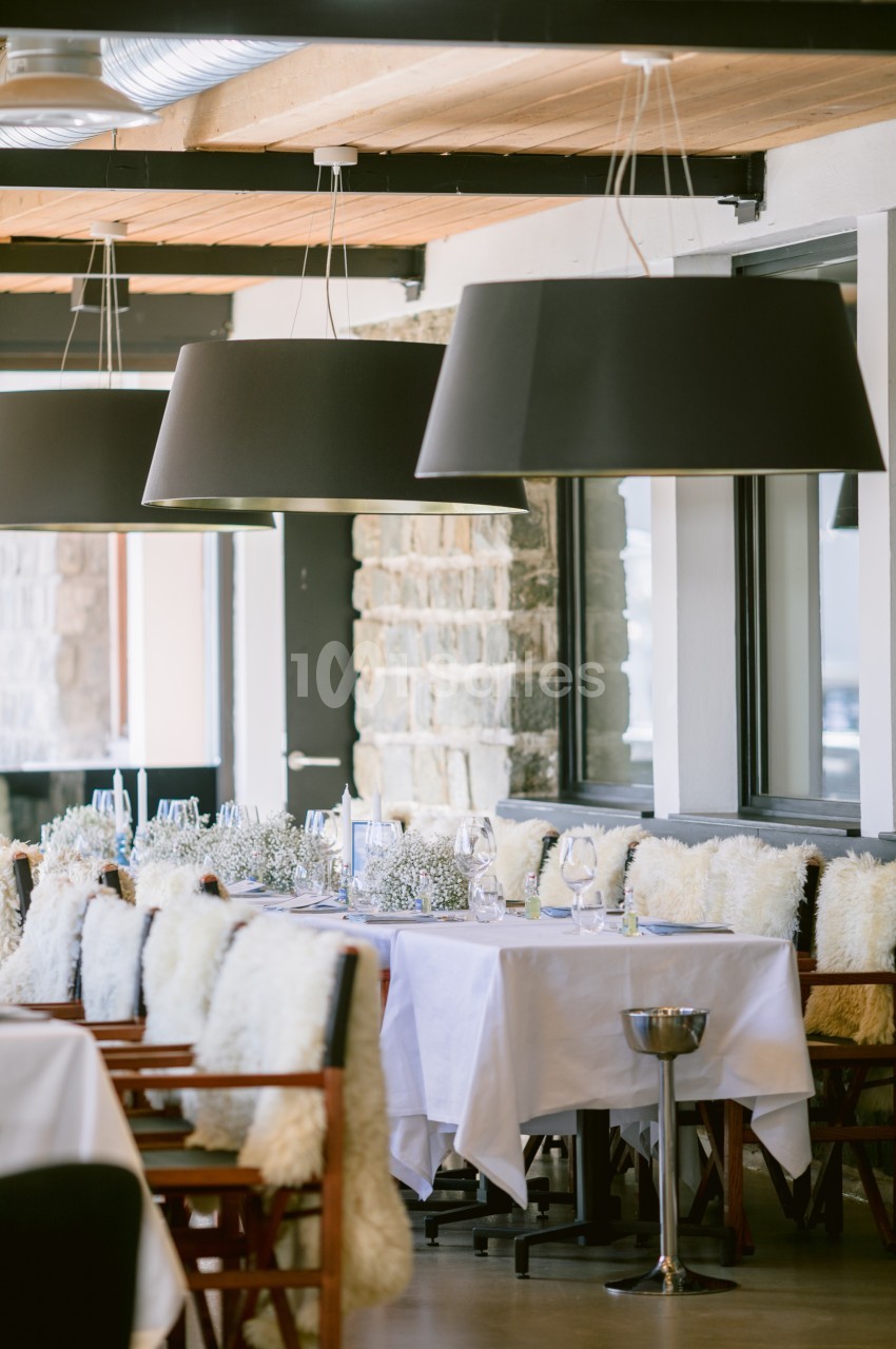 Salle de restaurant lumineuse avec tables dressées, chaises couvertes de fourrure et suspensions noires modernes.
