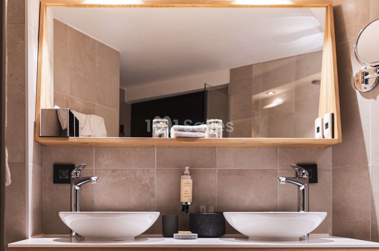 Deux lavabos blancs avec robinets modernes devant un grand miroir encadré en bois dans une salle de bain lumineuse.