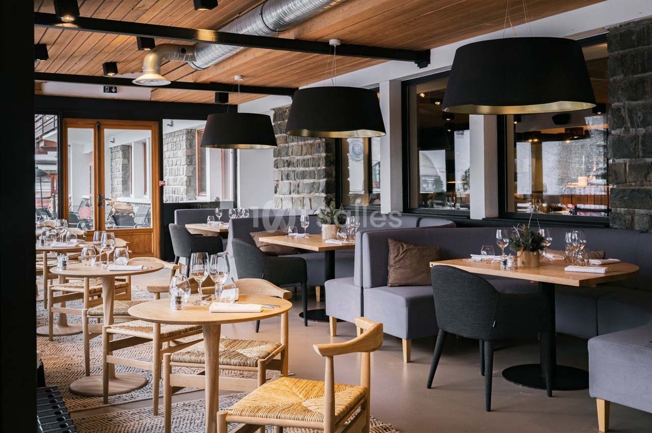 Salle de restaurant moderne avec tables en bois, chaises assorties et luminaires suspendus dans un cadre chaleureux.