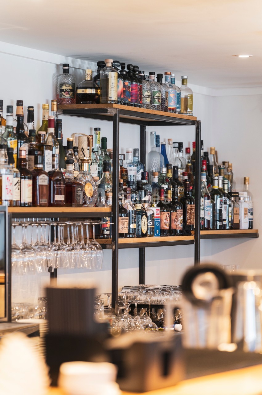 Étagères remplies de bouteilles d'alcool variées dans un bar, avec des verres suspendus en dessous.